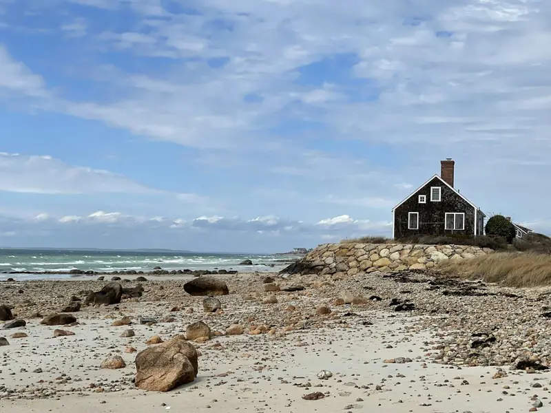 Dark-shingled house above a rocky beach